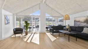 A spacious living area with a large glass door leading to an outdoor patio, a black sofa, a coffee table, and a hanging light fixture.