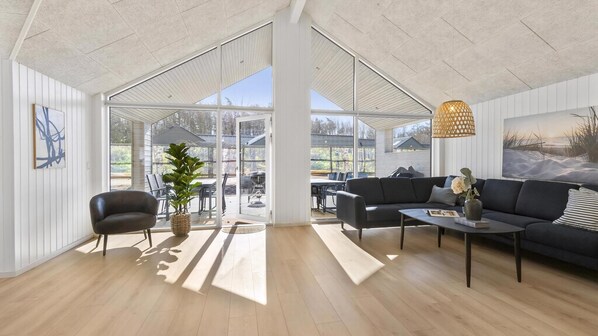 A spacious living area with a large glass door leading to an outdoor patio, a black sofa, a coffee table, and a hanging light fixture.