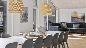 A modern dining area with a white table, grey chairs, and two hanging rattan lamps.