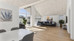 A spacious living area with a large window, a sofa set, and a dining table. - VillaVilla 824 - Fjellerup, Østjylland (Glesborg)