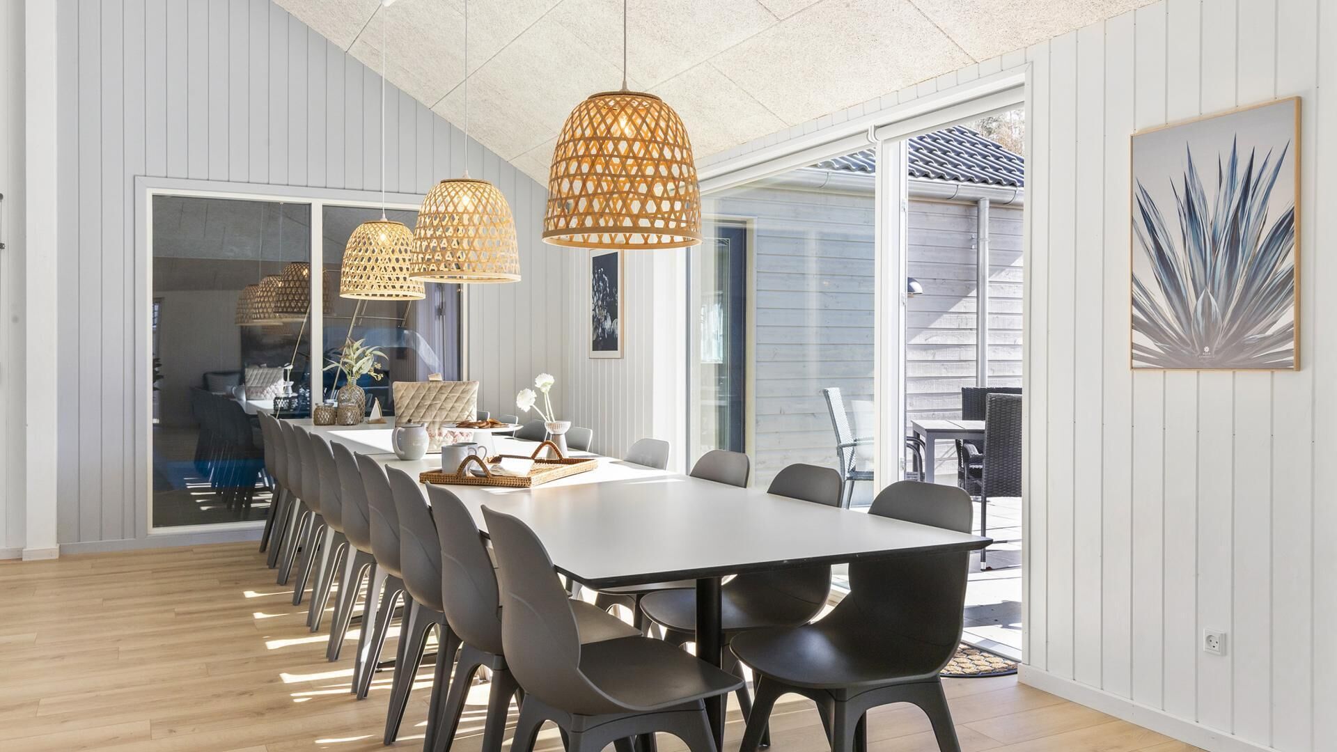 A modern dining area with a long table, multiple chairs, and pendant lights.