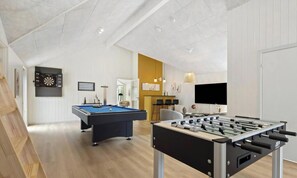 Ein modernes Wohnzimmer mit Billardtisch, Kicker und Fernseher.