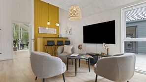 A modern living room with a flat-screen TV, grey armchairs, a coffee table, and a yellow accent wall. - VillaVilla 826 - Fjellerup, Østjylland (Glesborg)