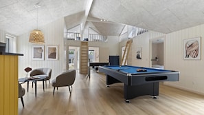 Amplia habitación con mesa de billar, zona de comedor con sillas y escalera que conduce a un nivel superior.