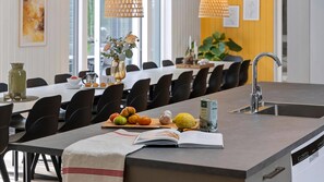 A modern dining area with a long table, chairs, a kitchen island with a sink, and a book on the table.