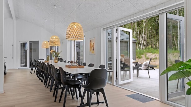 Een ruime eetruimte met een lange tafel, zwarte stoelen en hanglampen.