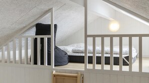 A loft bedroom with a sloped ceiling, a bed, a black chair, and a wooden bench.