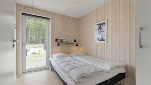 A bedroom with a bed, a door leading to a balcony, a wall-mounted shelf with items, and a framed picture.