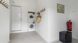 A laundry room with a white refrigerator, stacked washer and dryer, a fire extinguisher, and a wall-mounted hook system.