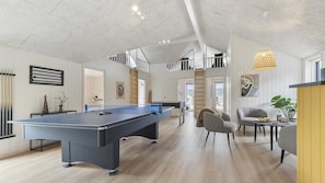 A spacious indoor area with a pool table, seating, and a staircase leading to an upper level.