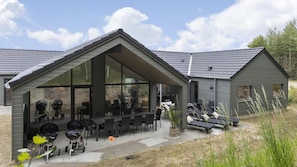 A modern house with a covered patio, outdoor seating, and a barbecue grill.