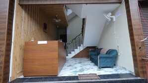 A reception area with a wooden desk, a blue sofa, a staircase, and a fan. - Shri Bala ji Dham (Mathura)