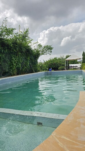 En swimmingpool med klart vatten, omgiven av grönska och ett vitt tält.