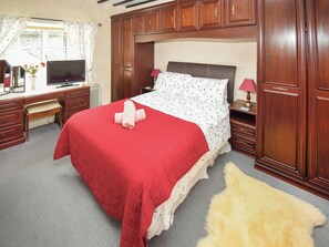 Une chambre à coucher avec un lit, une armoire en bois, un bureau avec un ordinateur et une fenêtre avec des rideaux.