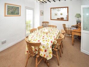 Une salle à manger avec une table ronde recouverte d’une nappe à motifs de fruits, entourée de chaises en bois.