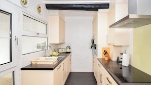 A narrow kitchen with light-colored cabinets, a black countertop, and a central island with a sink.