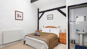 A bedroom with a bed, a nightstand, a dresser, a radiator, and a bathroom with a sink and mirror.