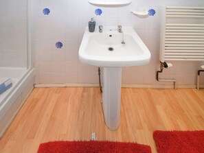 Une salle de bain avec un lavabo sur pied blanc, une baignoire blanche et un plancher en bois.