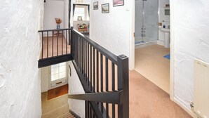 A staircase with a black railing leading to a room with a window, a chair, and a vase on a table.
