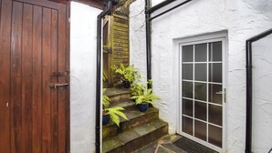 A stone-floored outdoor area with a wooden door, a set of steps leading to a white door, and a metal table.