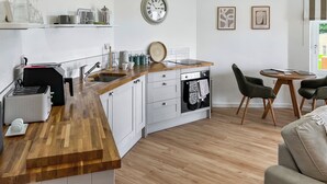 A modern kitchen with a wooden countertop, a sink, and a clock on the wall. There are two chairs and a small table in the dining area.