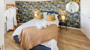 A neatly made bed with a blue headboard, a wooden side table with a lamp, and a mirror on the wall.