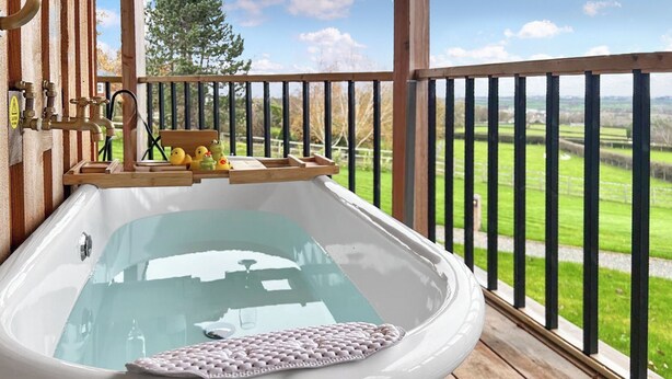 A bathtub on a wooden deck with a view of a green landscape.