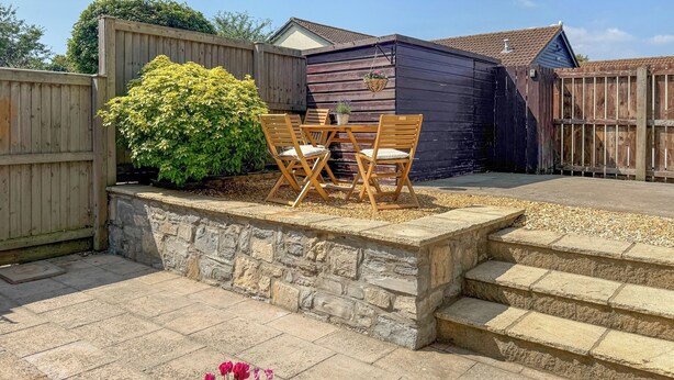 A patio with stone steps, a wooden table with chairs, a potted plant, and a wooden fence. - The Swallows - UK50177 (Stoke St. Gregory, near Taunton)