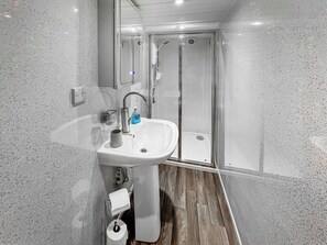 A modern bathroom with a white sink, a glass shower enclosure, and a wooden floor.