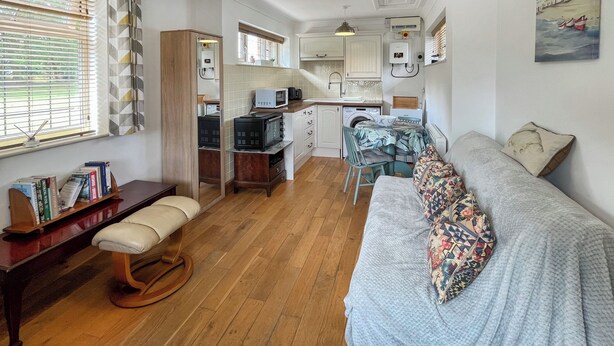 Un espacio habitable compacto con kitchenette, un sofá, un banco de madera y una mesa de comedor.