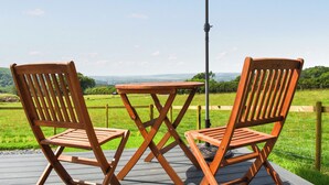 Zwei Holzstühle und ein Tisch auf einer Terrassenförmigen Veranda mit Blick auf eine grüne Landschaft.