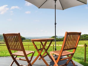 Dos sillas de madera y una mesa en una terraza con vistas a un paisaje verde.