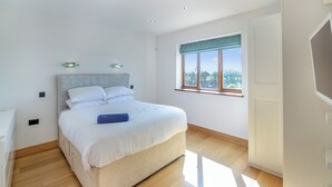 Ein Schlafzimmer mit Bett, Holzdielen, einem Fenster mit Ausblick und eingelassenen Deckenleuchten.