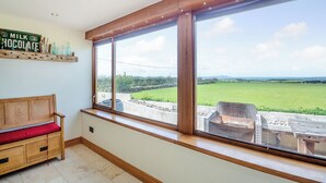 Ein Zimmer mit großem Fenster mit Blick auf ein grünes Feld, einer hölzernen Bank und einem Regal mit alten Milch- und Schokoladenflaschen.