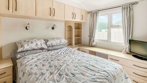 A bedroom with a bed, built-in wardrobe, bedside tables, a TV, and a window with curtains. - 3 bedroom accommodation in Hogsthorpe (Hogsthorpe)