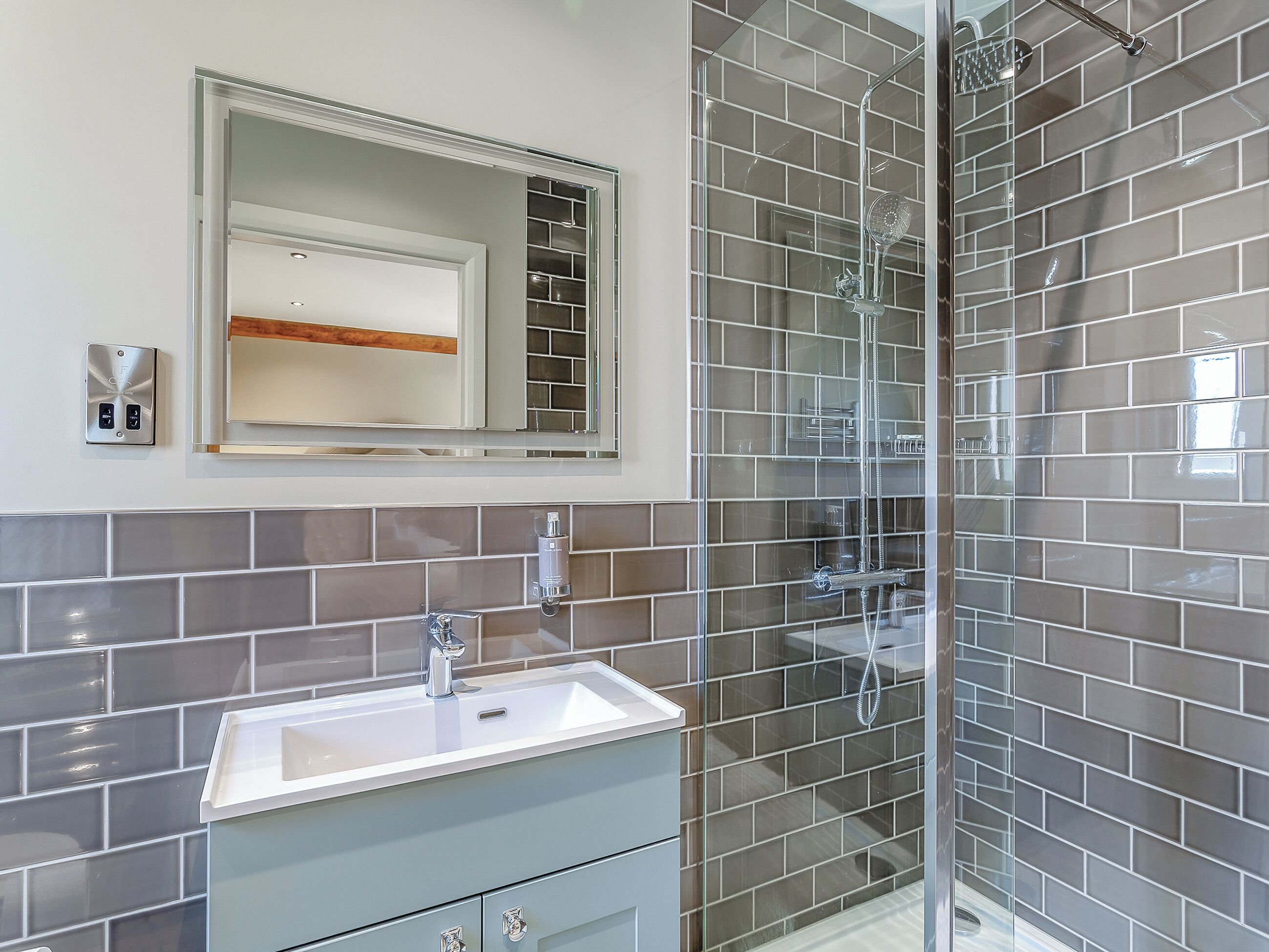 Une salle de bain avec une douche à parois de verre, un lavabo blanc et un miroir au-dessus.