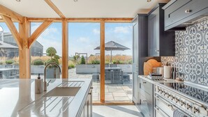 A modern kitchen with a large island, dark cabinetry, and a view of the outdoor patio. - 5 bedroom accommodation in Ryther (Ryther)