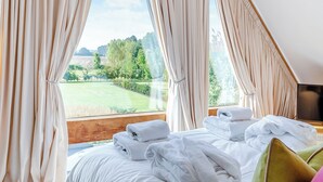 A bedroom with a bed, white towels, and a view of a green landscape through curtains. - 5 bedroom accommodation in Ryther (Ryther)
