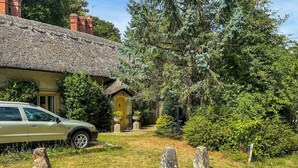A house with a thatched roof, a car parked in front, and a well-maintained garden with stone pillars and a yellow door. - 3 bedroom accommodation in Tisbury (Tisbury)
