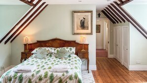 A bedroom with a bed, two bedside tables, a wooden headboard, a framed picture on the wall, and a staircase leading to another room. - 3 bedroom accommodation in Tisbury (Tisbury)