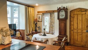 A dining area with a round table, wooden chairs, a clock, and a wooden door. - 3 bedroom accommodation in Tisbury (Tisbury)