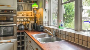 A kitchen with a sink, two ovens, a coffee maker, and a window with a view of greenery. - 3 bedroom accommodation in Tisbury (Tisbury)