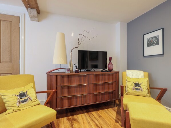 Un salon avec un meuble en bois, deux fauteuils jaunes ornés de motifs d’abeilles, un téléviseur et un vase.