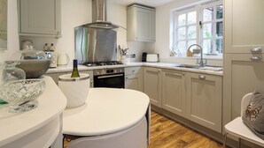 A modern kitchen with a gas stove, oven, and stainless steel range hood. There is a window with a view of greenery outside.