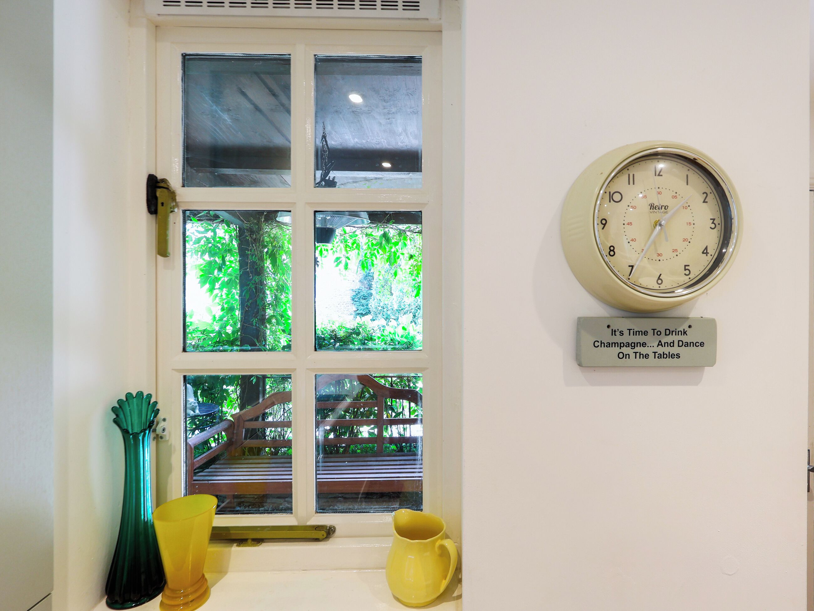 Una habitación con una ventana, un reloj y un cartel que dice 'Es hora de tomar champán... y bailar sobre las mesas'.