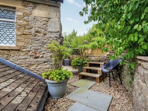 Un bâtiment en pierre avec une fenêtre, un banc en bois, une plante en pot et une chaise noire.
