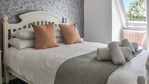 A neatly made bed with white and brown bedding, a grey herringbone throw blanket, and a window with a view of trees. - 3 bedroom accommodation in Southrepps (Southrepps)