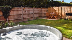A hot tub in a backyard with a wooden fence, a table, and chairs. - 3 bedroom accommodation in Southrepps (Southrepps)