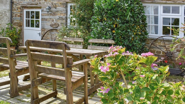 Un bâtiment en pierre avec un banc en bois et une brouette.