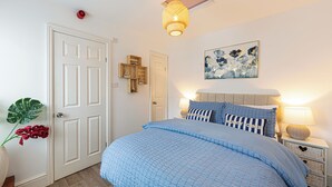 Een slaapkamer met een groot bed, een nachtkastje met een lamp, een wandplank met decoratieve objecten en een plafondlamp.